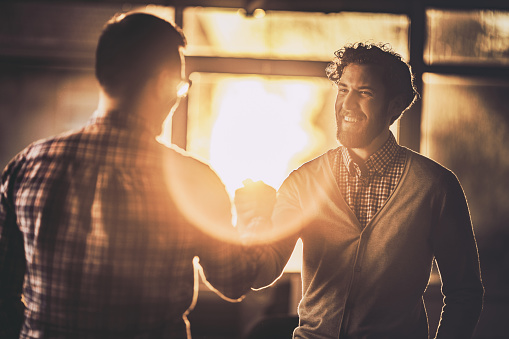 Happy businessmen greeting each other with a manly handshake in the office at sunset.