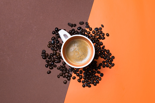 A top view of a fresh espresso cup surrounded by coffee beans on orange and brown split background