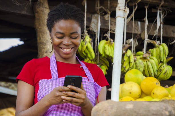 une jeune femme du marché africain se sent heureuse de ce qu’elle a vu sur son téléphone portable - country market photos et images de collection