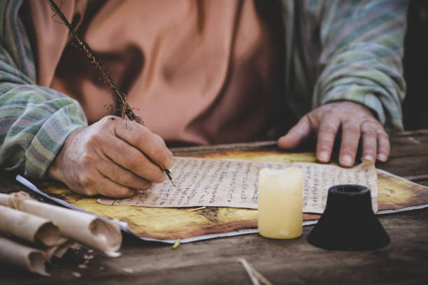 istock Closeup of man in a robe writing on old paper scrolls 1438317395