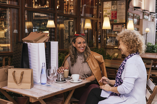 A shallow focus shot of two adult cheerful women with shopping bags having coffee and tea in a cafe
