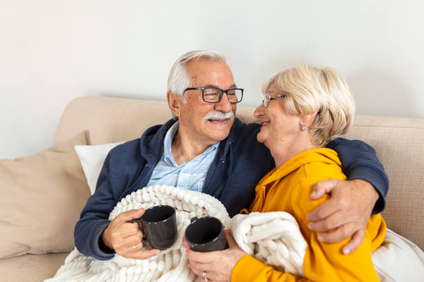 istock Happy old couple sitting on the sofa. Feeling cozy,drinking coffee or tea 1438318063