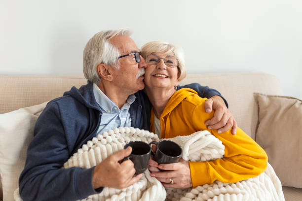 Happy old couple sitting on the sofa. Feeling cozy,drinking coffee or tea