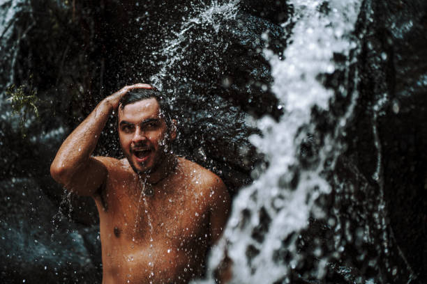 istock Caucasian male wearing a swimsuit and standing under waterfall 1438320627