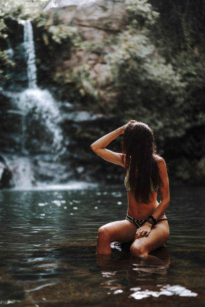 istock Young Caucasian female sitting on a rock in a river surrounded by beautiful greenery 1438320794