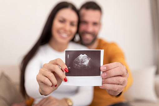 Woman and her boyfriend holding up an image of her sonogram of the baby. Young happy Couple with baby ultrasound photo