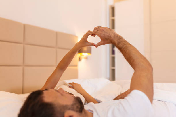 istock Couple Lying On Bed Forming Heart Shape With Hand 1438323717