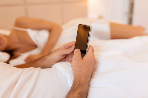 tradire l'uomo infedele sdraiato con l'amante nel letto dell'hotel. chiama dalla finace al cellulare. imbroglione ha una relazione con un amante segreto e una relazione con un'altra donna. infedeltà e triangolo amoroso. - sensuality people mobile phone 30s foto e immagini stock