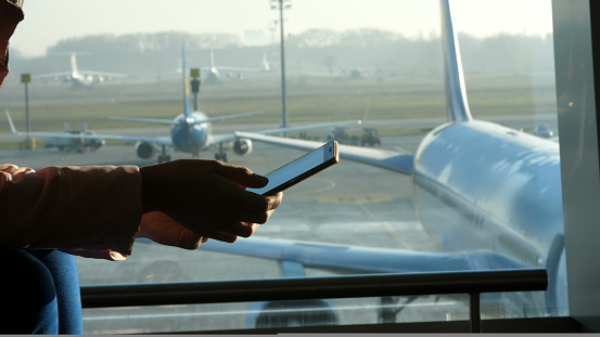 close-up, at the airport, in the waiting room, against the background of a window overlooking the airplanes and the runway, silhouettes of female hands holding smartphone. High quality photo