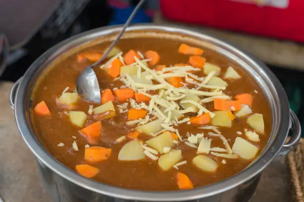 A large bowl of beef mechado sprinkled with cheese. With beef chunks and chopped potatoes and carrots. For a catered event.