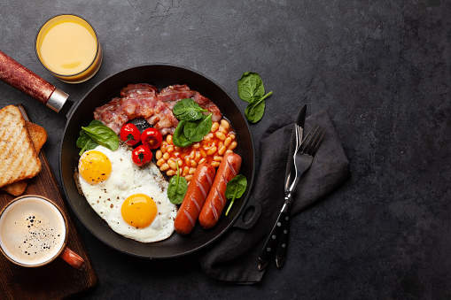 English breakfast with fried eggs, beans, bacon and sausages. Top view flat lay with copy space