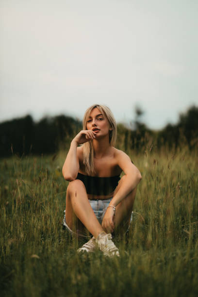 Portrait of a beautiful young blond-haired woman sitting in the field and enjoying a lovely summer day