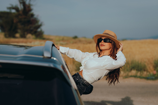 Beautiful young fashionable woman relaxing and enjoying a road trip on a sunny summer day in nature