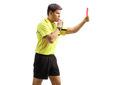 Profile shot of a football referee blowing a whistle and showing a red card isolated on white background