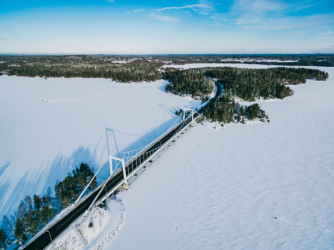 Aerial view of white cable-stayed bridge with snow lakes и green woods in Finland, winter landscape