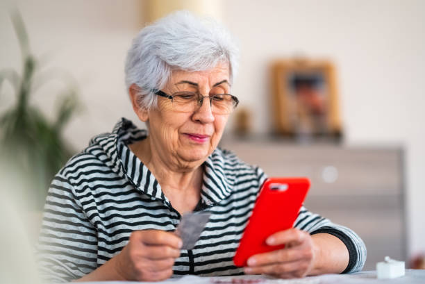 istock Senior woman using mobile phone at home with medicine pills 1438335792