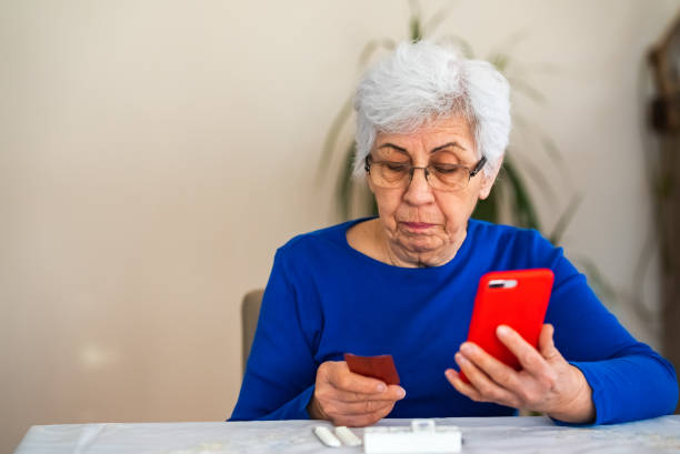istock Senior woman using mobile phone at home with medicine pills 1438335814