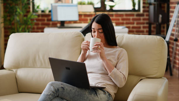 istock Happy asian woman sipping beverage while working remotely on laptop 1438335820