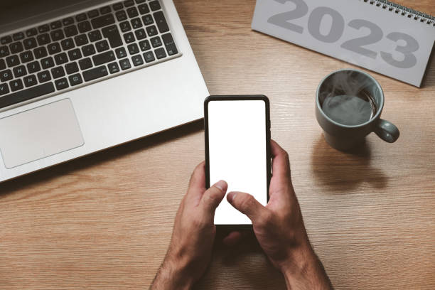 istock Unrecognizable man holding a smartphone with a blank screen, a laptop and a hot coffee - concept goals and action plan, new year 1438337811