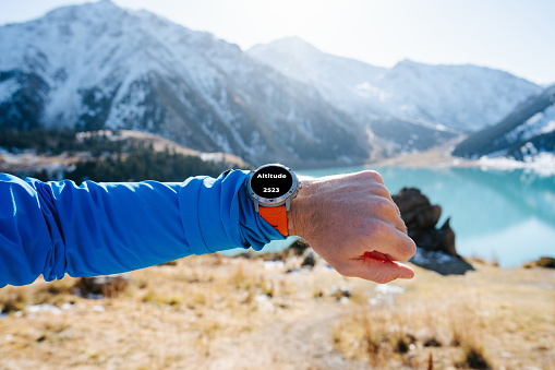 istock Male hand with smartwatch showing an altitude. Beautiful mountain lake in back 1438340621