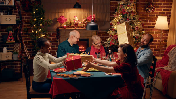 istock Joyful people gathered at Christmas dinner table while exchanging gifts 1438341541