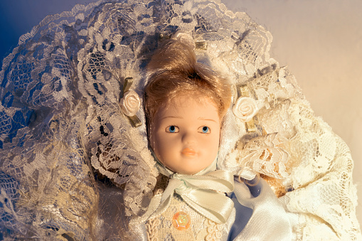 Portrait of collectible porcelain doll wearing period clothing with blond hair, headdress and blue eyes