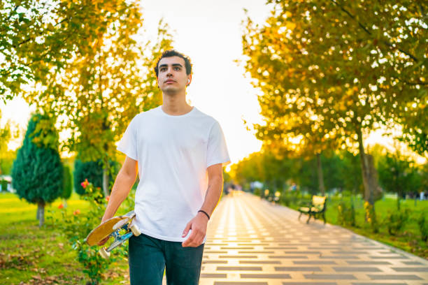 istock Young man with skateboard walking in public park 1438345949