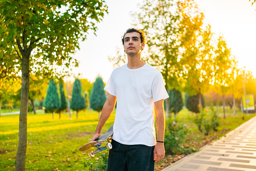Young man with skateboard walking in public park