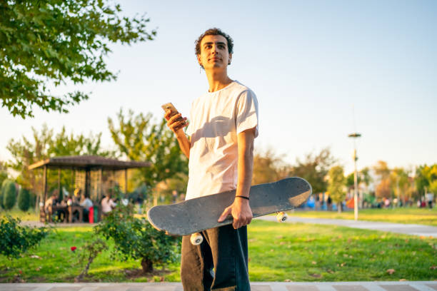 istock Young man with skateboard using phone at public park 1438345983