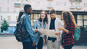 istock Young men and women with backpacks are looking at map standing in the street in foreign city and talking discussing journey. Navigation, youth and tourism concept. 1438349392