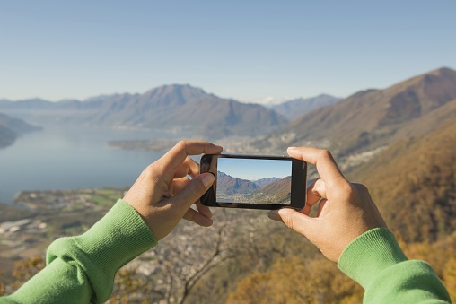 A person taking a picture of the Maggiore Alpine Lake and mountains in Switzerland