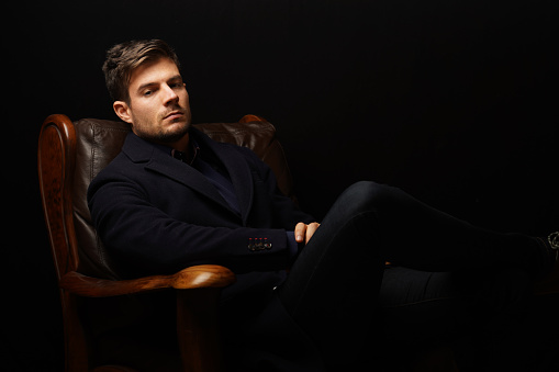 A portrait of a handsome well-dressed man sitting on a leather couch