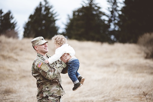 A shallow focus shot of a smiling American soldier carrying his baby
