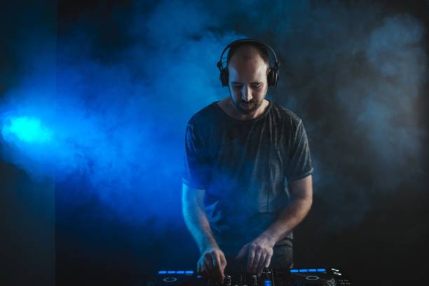 istock Male DJ working under the blue lights and smoke in a studio against a dark background 1438351308