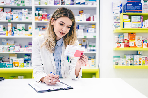Young pharmacist woman working, writing down something