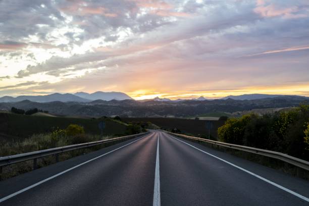 istock Empty highway surrounded by hills under the cloudy sunset sky 1438352975