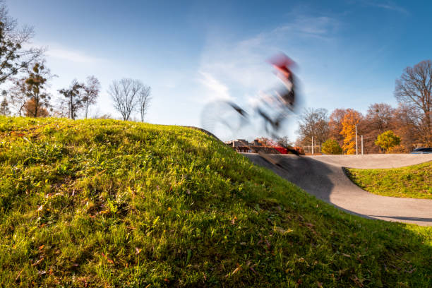 Blurred biker jumping on an asphalt pump track surrounded by nature on a sunny day. Extreme sport and great way to spend free time. Blurred biker jumping on an asphalt pump track surrounded by nature on a sunny day. Extreme sport and great way to spend free time. bmx racing stock pictures, royalty-free photos & images