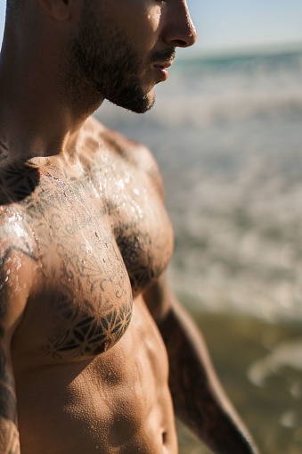 The vertical partial view of an attractive man at the beach with tattoo on his wet chest