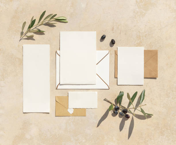 Blank paper cards on a concrete table decorated with olive branches with fruits top view, mockup. Sunny summer mediterranean scene with wedding stationery set. Flat lay with place for text