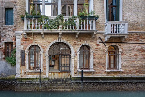 Venice, Italy - October 8th 2022:  Façade of a old house with doorway, stairs and windows facing a narrow canal in the center of the old and famous Italian city Venice