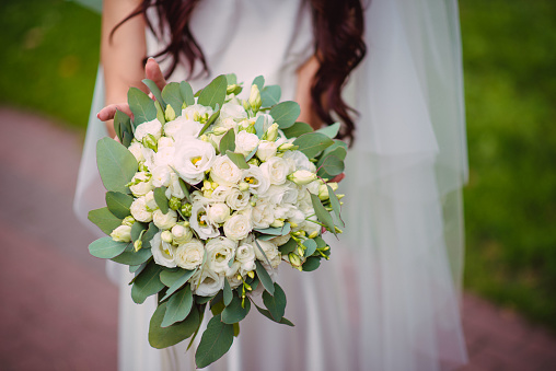 The bride holds a wedding bouquet from roses in her hands, wedding day flowers. Beautiful bohemian wedding flower bouquet. Girl in a dress with a bouqet of rose.