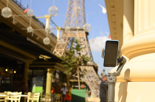 Israel Netivod, November 2022. Hand holding Gimbal DJI and iPhone SE against the background of the Eiffel Tower Replica of the Eiffel Tower in Israel. Travel concept, travel blog, influencer.