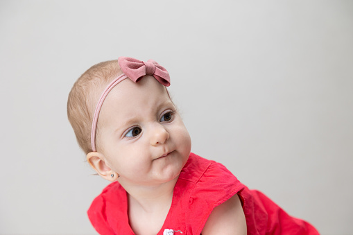 Portrait of a baby girl at eleven months old. The baby is wearing a red dress with a headband.