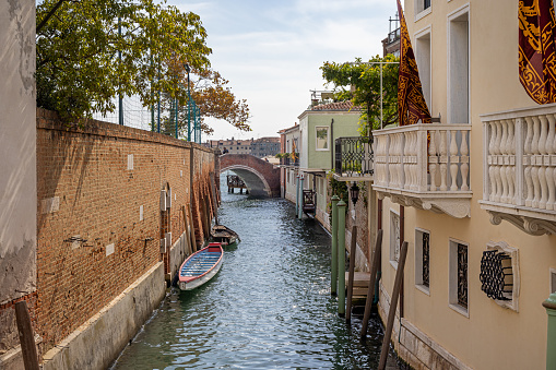 Venice, Italy - October 9th 2022: Narrow canal with moored wooden boats and a arch bridge in the center of the old and famous Italian city Venice