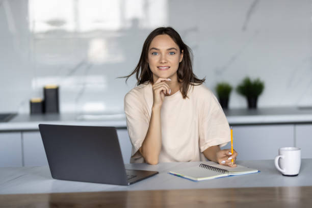 istock Beautiful happy woman drinking tea while working with laptop in kitchen 1438359182