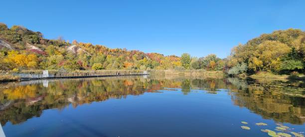 istock Panoramic view of a lake surrounded by autumn trees reflecting on water surface on a sunny day 1438359698