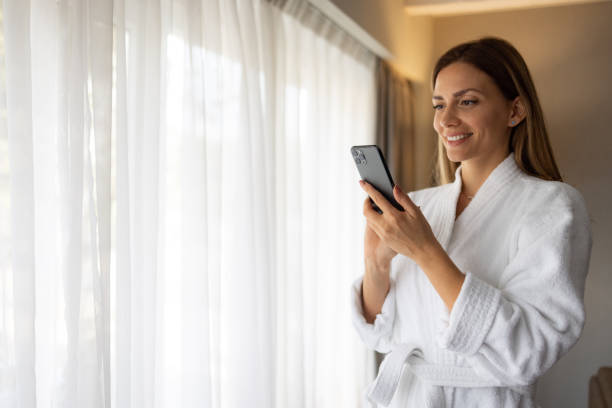 istock Smiling beautiful woman using her cellphone in her bathrobe 1438361454