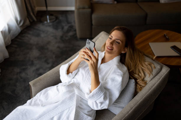 istock Smiling woman relaxingly lying on armchair, using her smart phone in bathrobe 1438361473