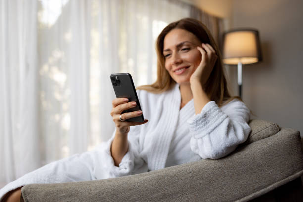 istock Smiling woman checking her mobile phone, relaxingly sitting in bathrobe 1438361483