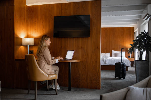 mujer en un viaje de negocios usando una computadora portátil en la habitación del hotel para trabajar - women computer home interior brown hair fotografías e imágenes de stock
